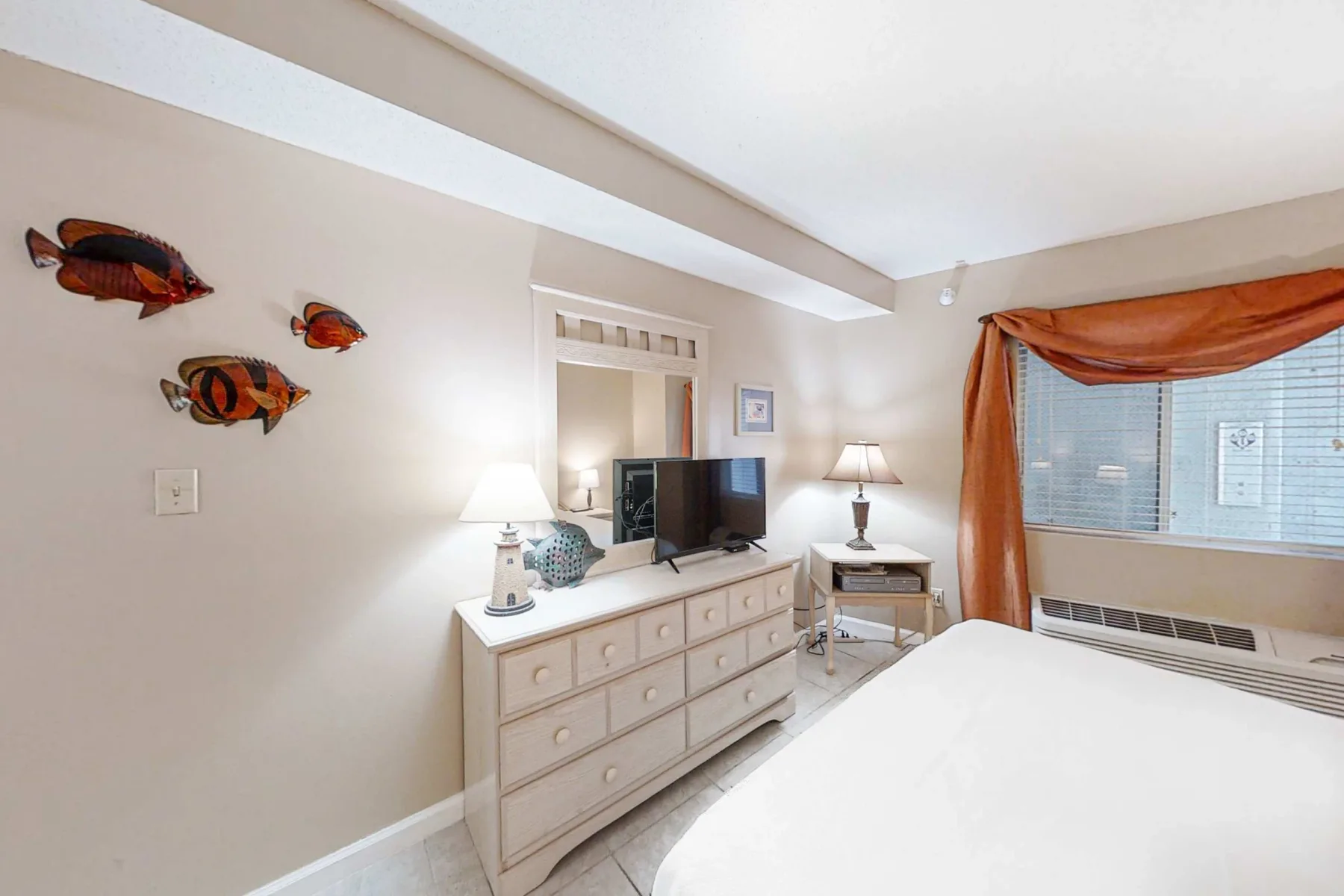 A bright bedroom with a bed, dresser, and window dressed with orange curtains.