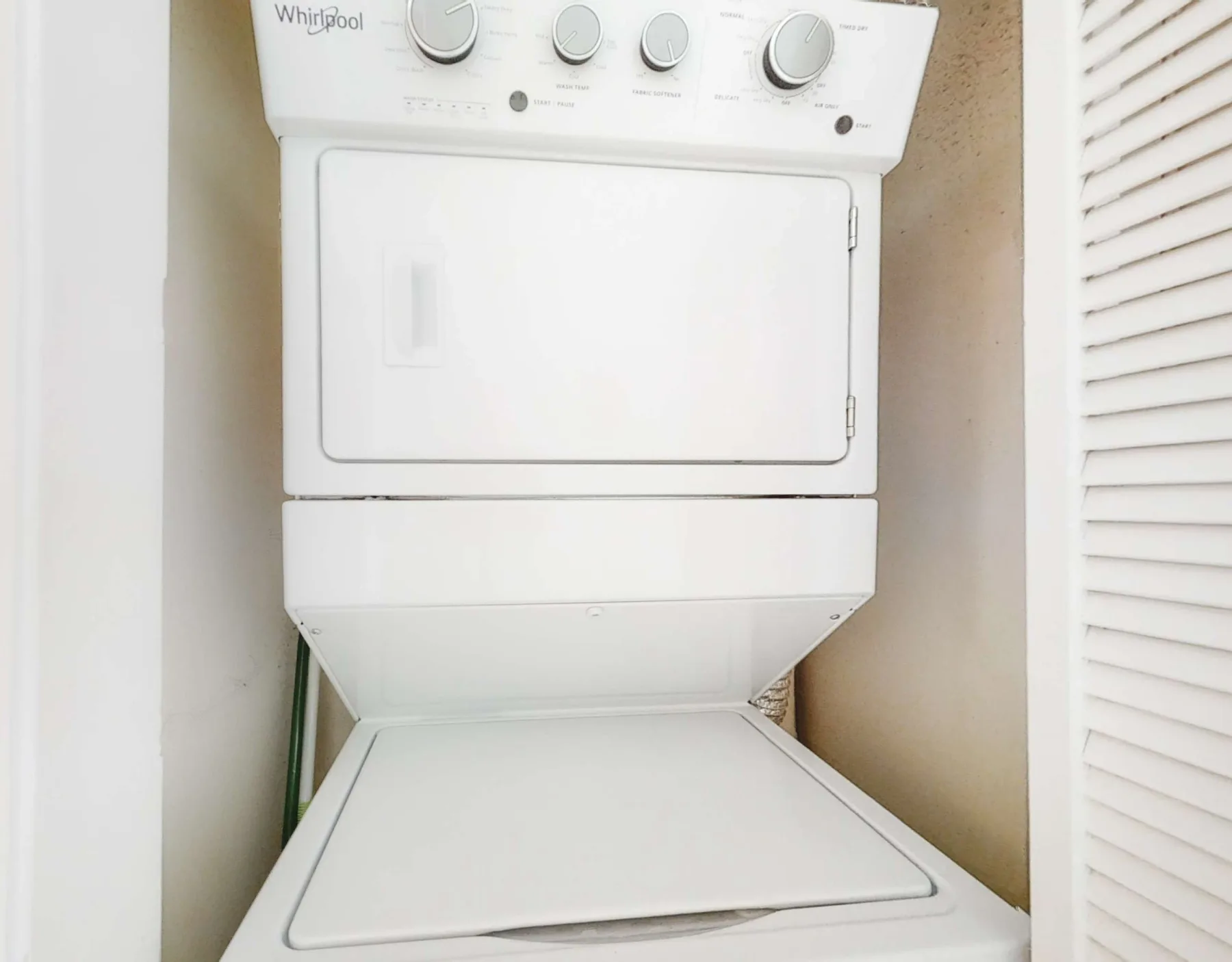 A stacked white washer and dryer are installed in a narrow laundry closet.