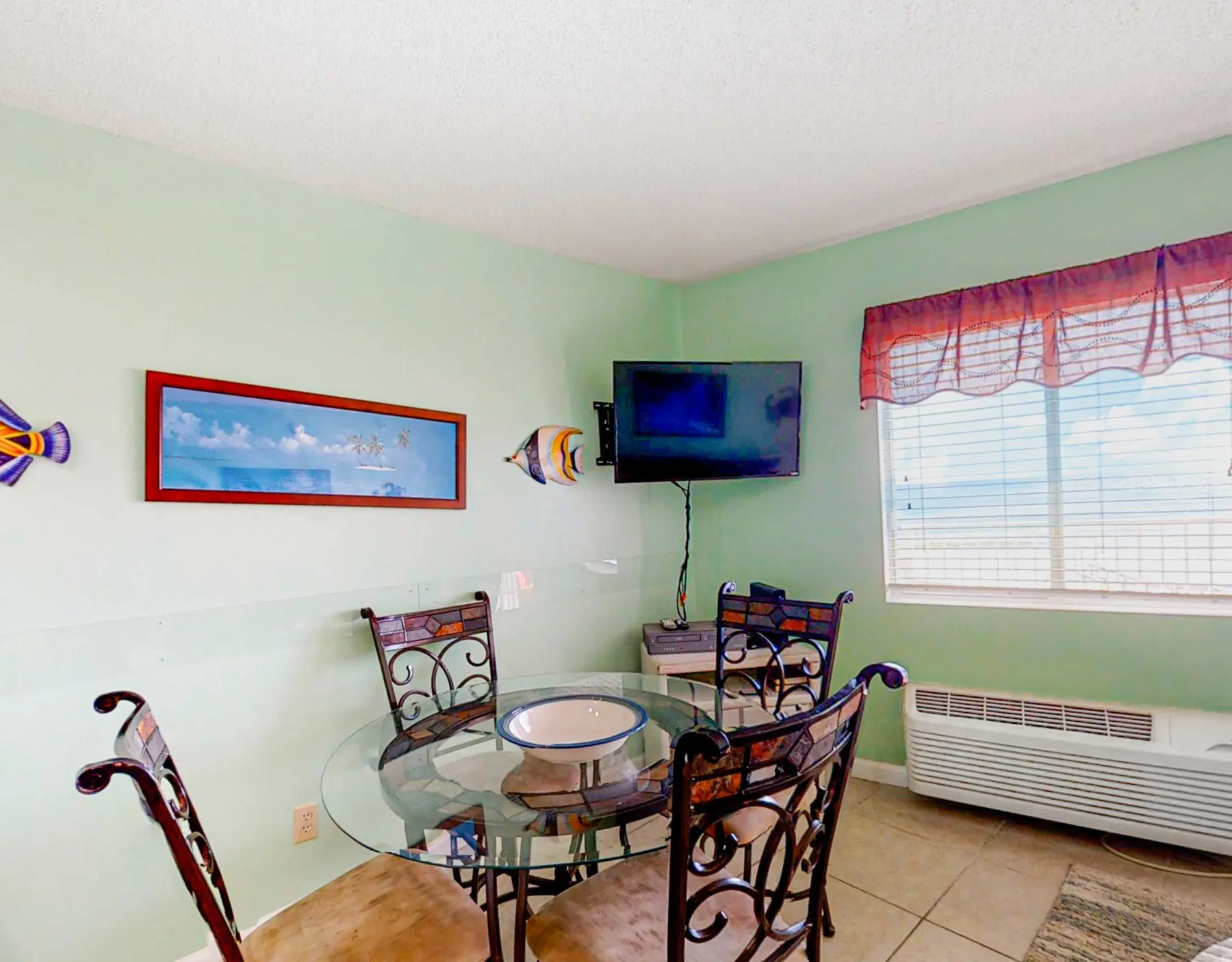 A dining area with a glass table and a wall-mounted television.