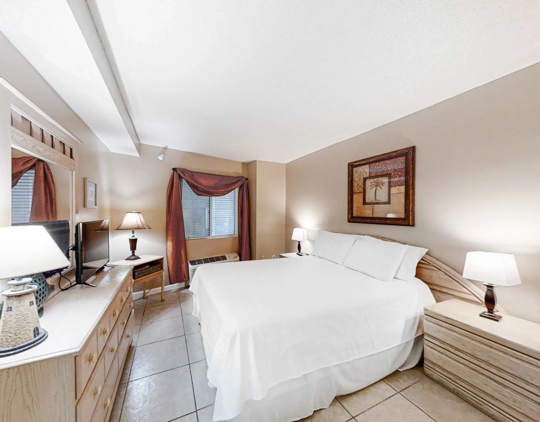 A bedroom with a neatly made bed, bedside tables, and a desk.