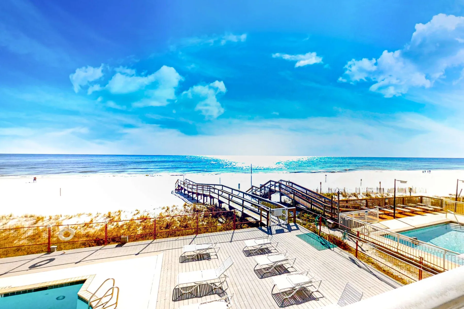 A seaside pool deck with lounge seating overlooks the ocean and a sandy beach.