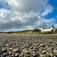 Representative hotel space: A rocky shoreline stretches toward a low coastal building beneath a cloudy sky.