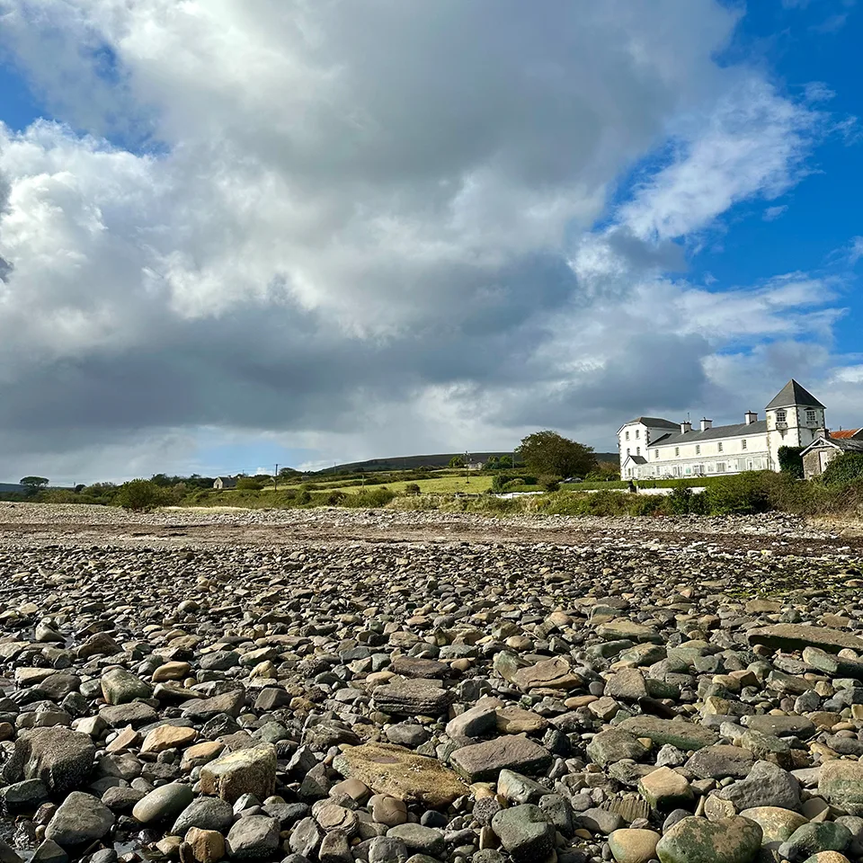 Representative hotel space: A rocky shoreline stretches toward a white building beneath a cloudy sky.