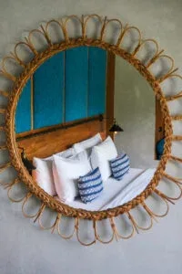 Espacio representativo del hotel: Un dormitorio reflejado en un espejo redondo tejido, con ropa de cama blanca y detalles azules.