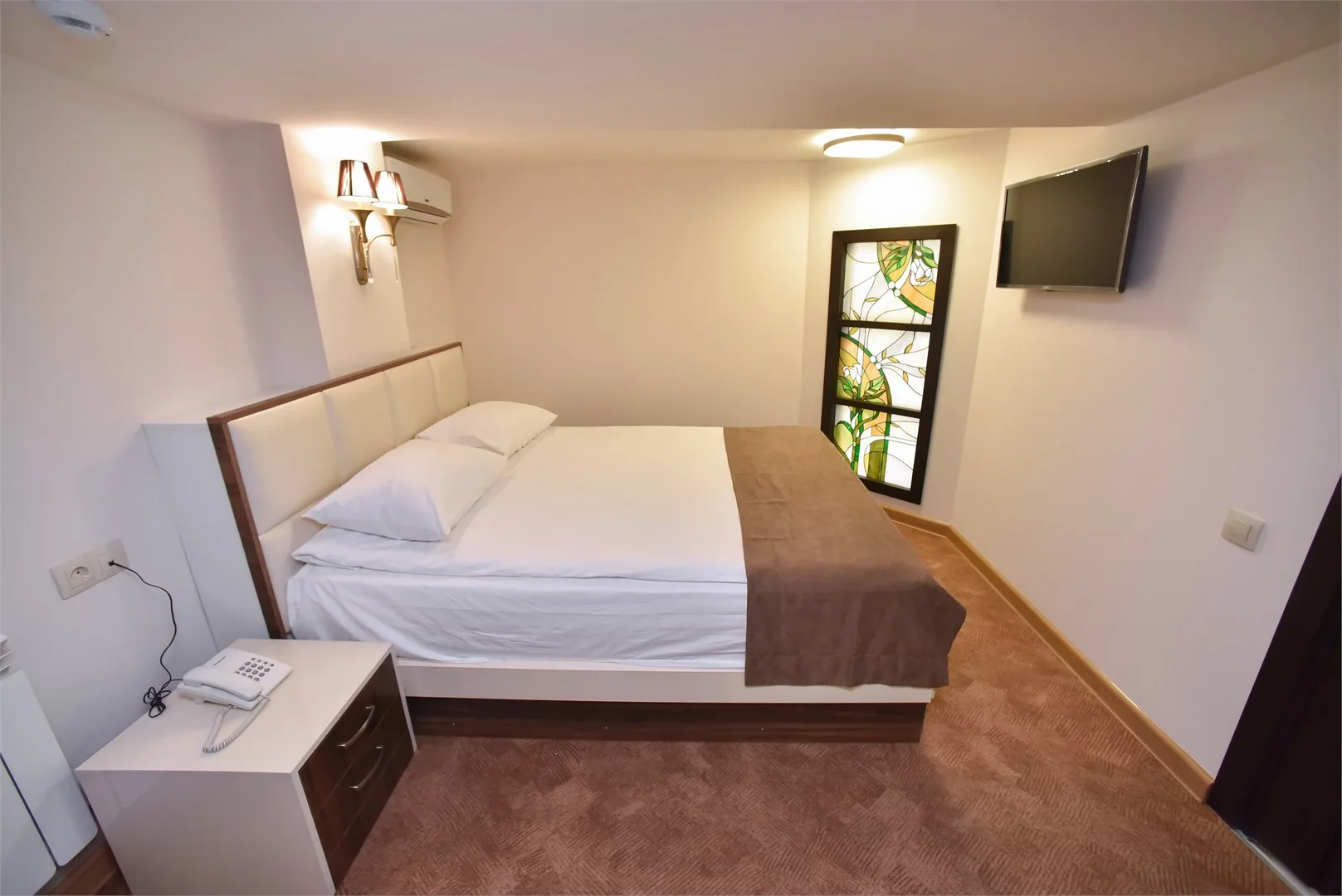 Representative hotel space: A bedroom with a neatly made bed and a wall-mounted television.