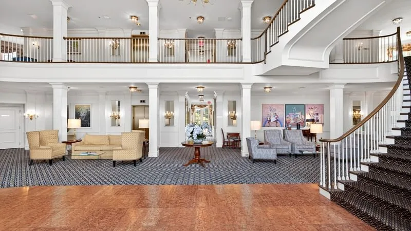 Espacio representativo del hotel: Un amplio vestíbulo de hotel con asientos, una mesa central y una escalera curva.