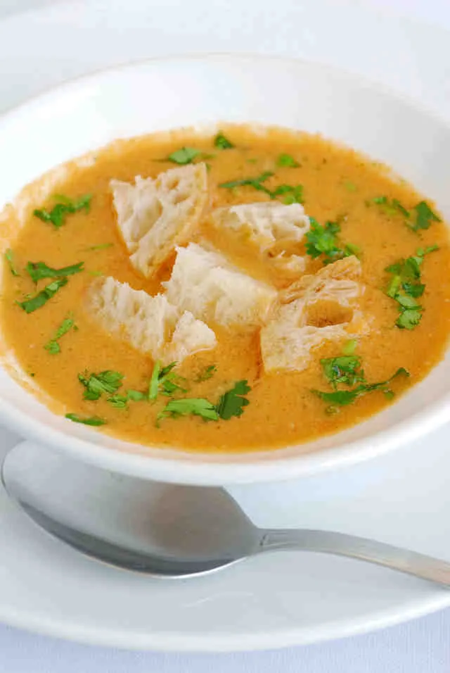 Representative hotel space: A bowl of orange soup topped with herbs and pieces of bread.