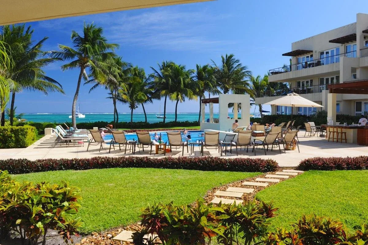 Espacio representativo del hotel: Zona de piscina con asientos, palmeras y el océano al fondo.