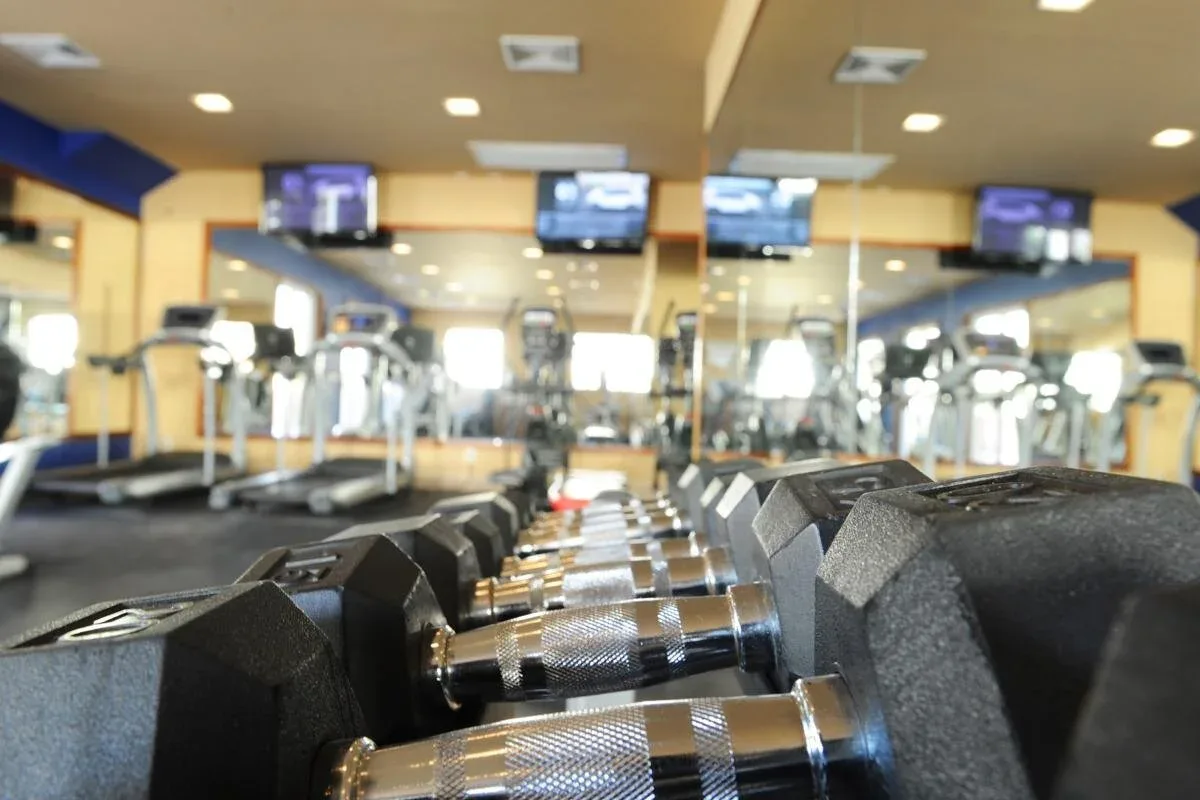 Espacio representativo del hotel: Un gimnasio con filas de mancuernas en primer plano y máquinas de ejercicio detrás.