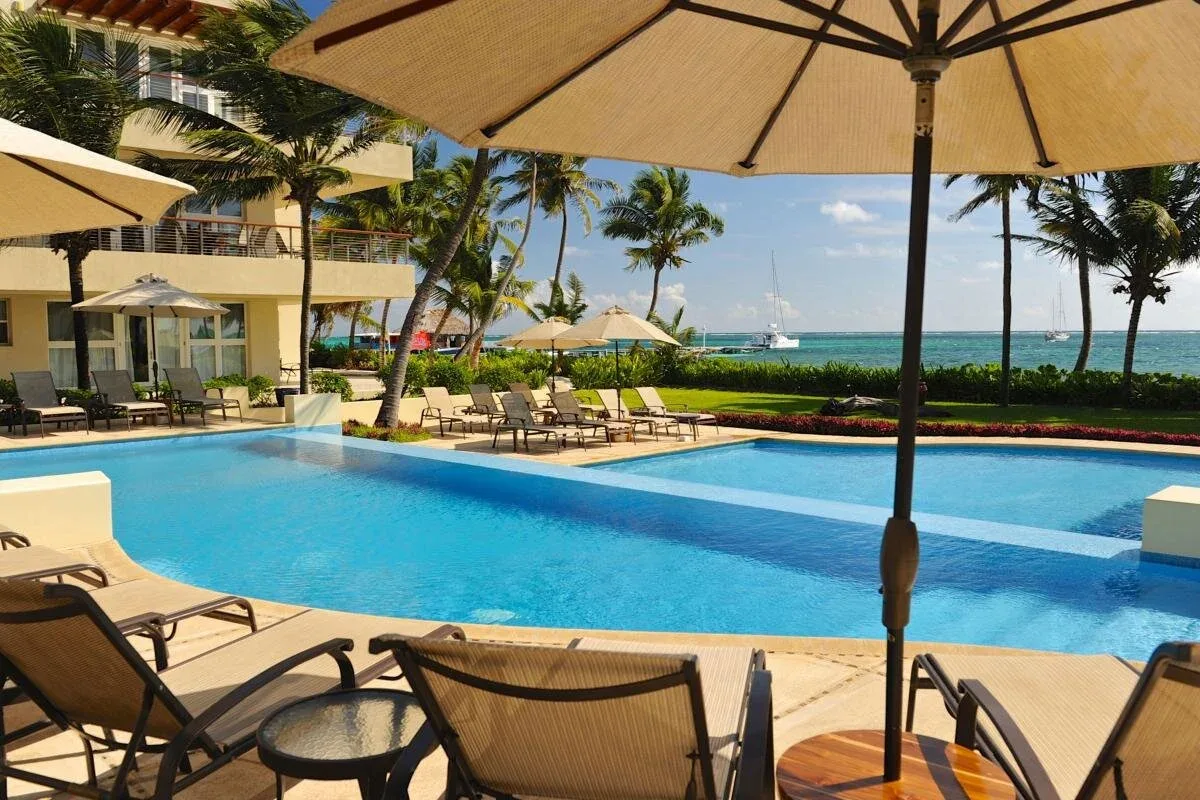 Espacio representativo del hotel: Una piscina al aire libre con asientos, palmeras y el mar al fondo.