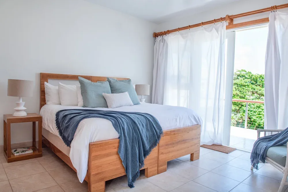 Espacio representativo del hotel: Un dormitorio luminoso con una cama de madera y cortinas junto a una puerta de vidrio.