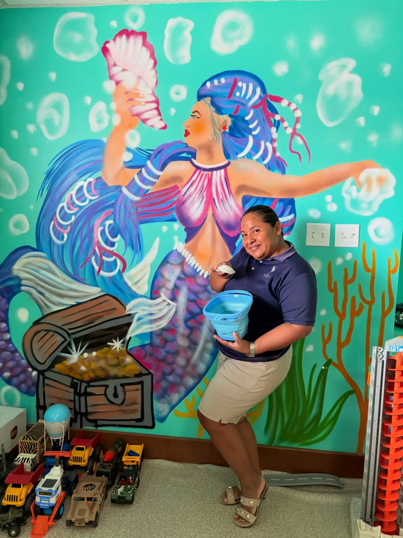 Espacio representativo del hotel: Una persona está junto a vehículos de juguete frente a un mural submarino colorido.