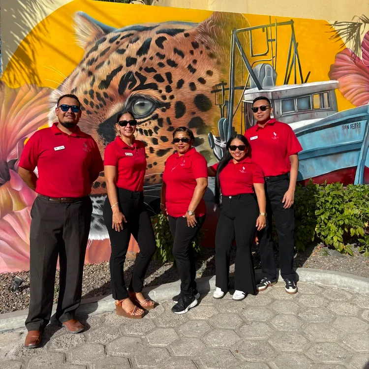 Espacio representativo del hotel: Cuatro personas con camisas rojas posan frente a un mural colorido al aire libre.