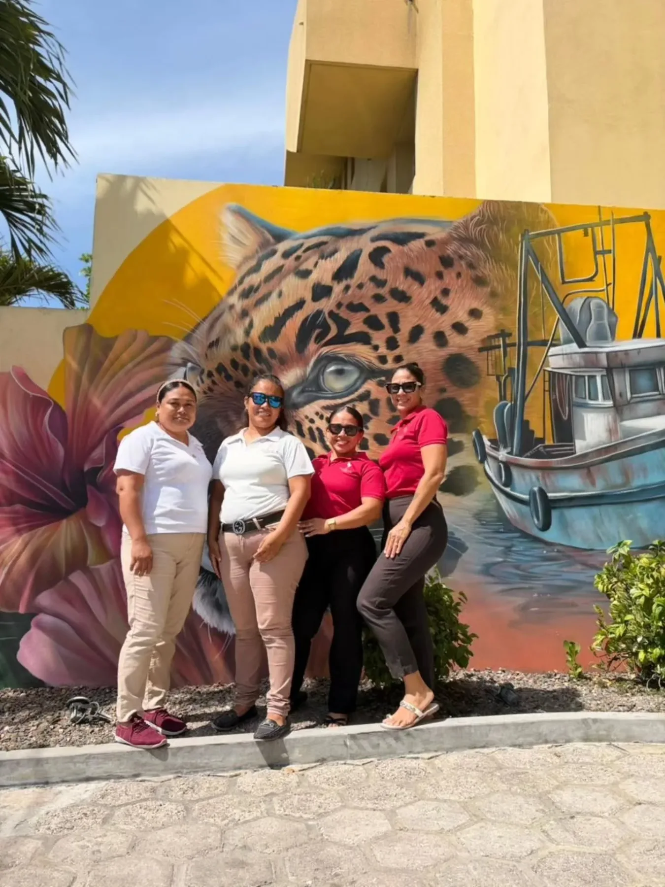 Espacio representativo del hotel: Cuatro personas posan frente a un mural colorido con un felino moteado y un barco.