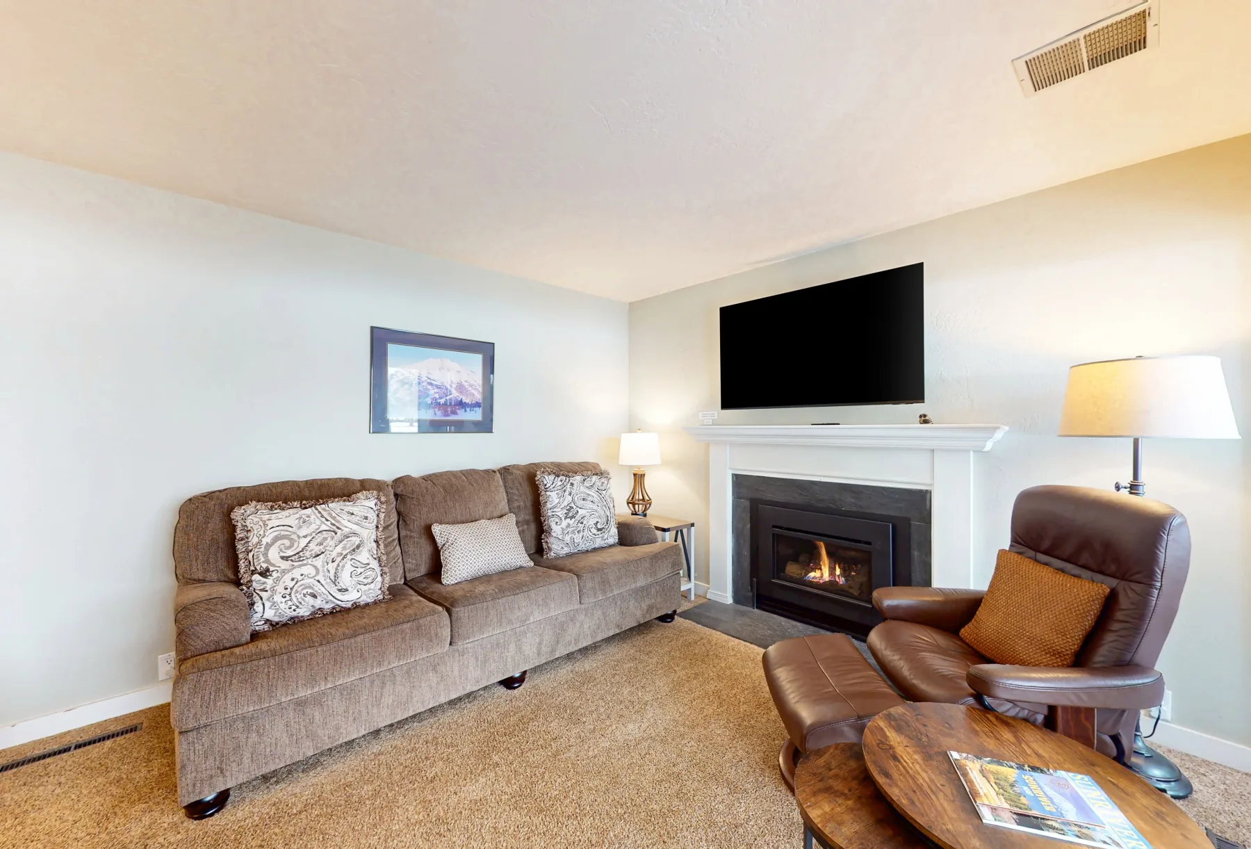 Una sala de estar con sofá, sillón y televisor sobre la chimenea.