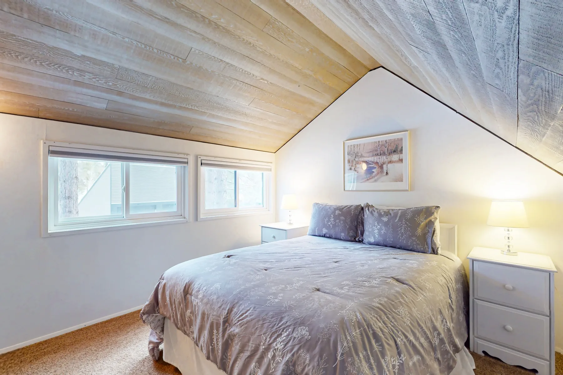 Un dormitorio luminoso con una cama grande bajo un techo inclinado y ventanas.