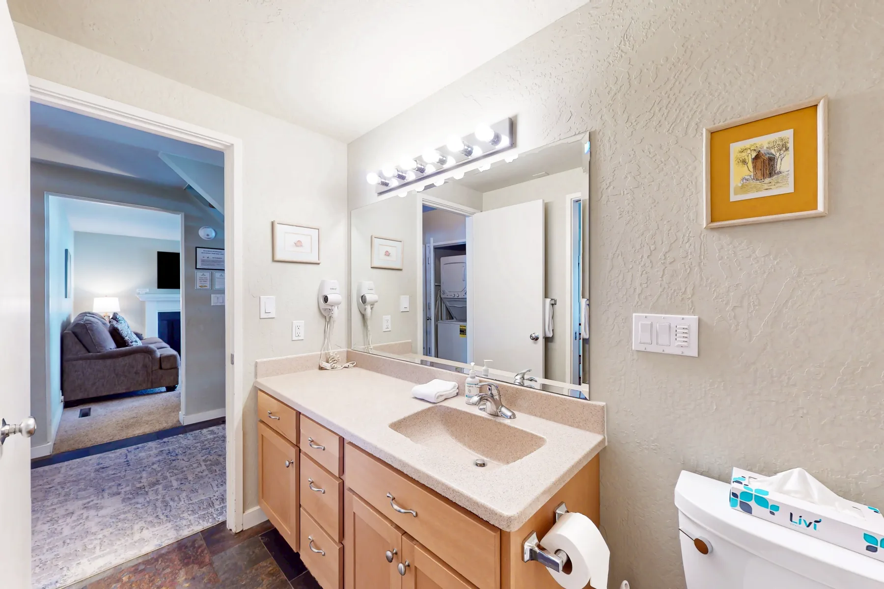 Un tocador de baño con lavabo y un espejo grande junto a una puerta abierta.