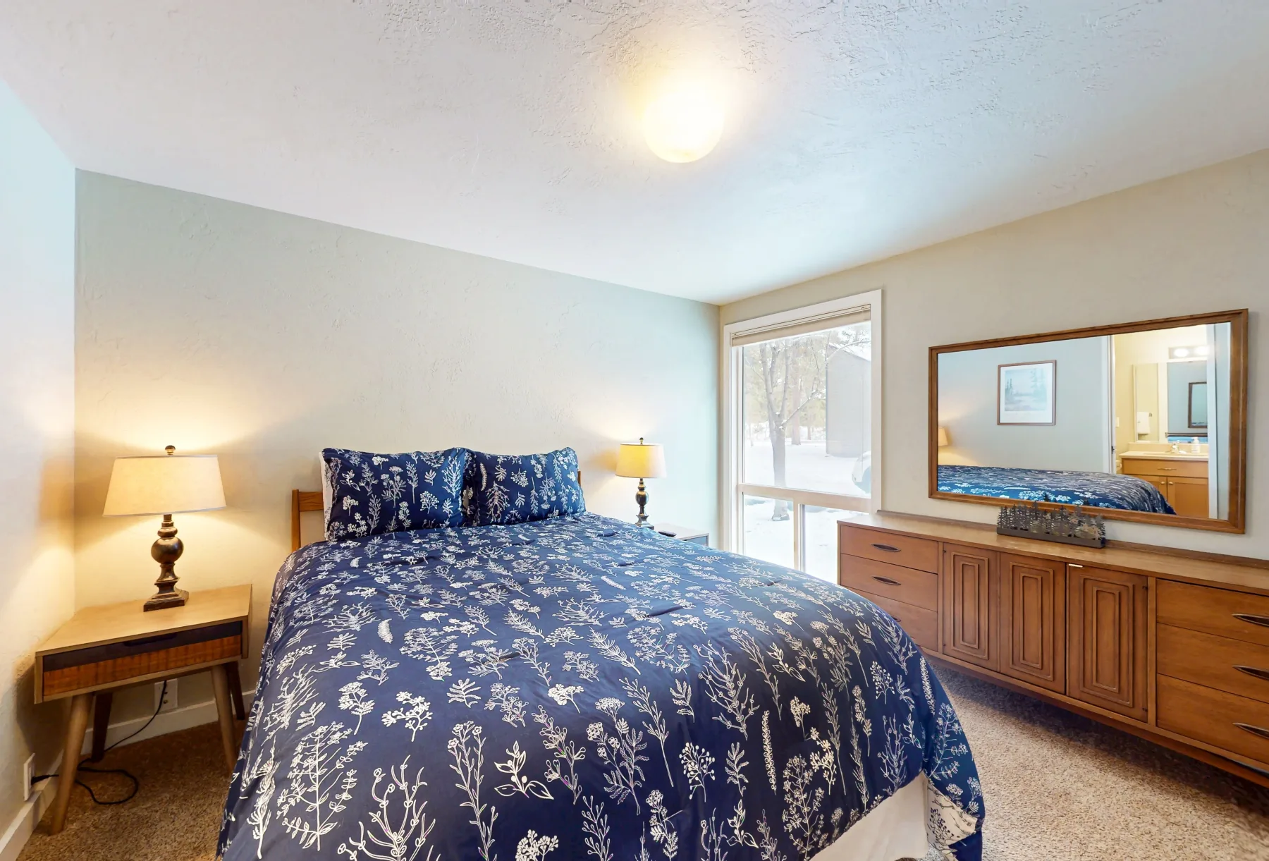 Un dormitorio con una colcha azul floral y una cómoda de madera.