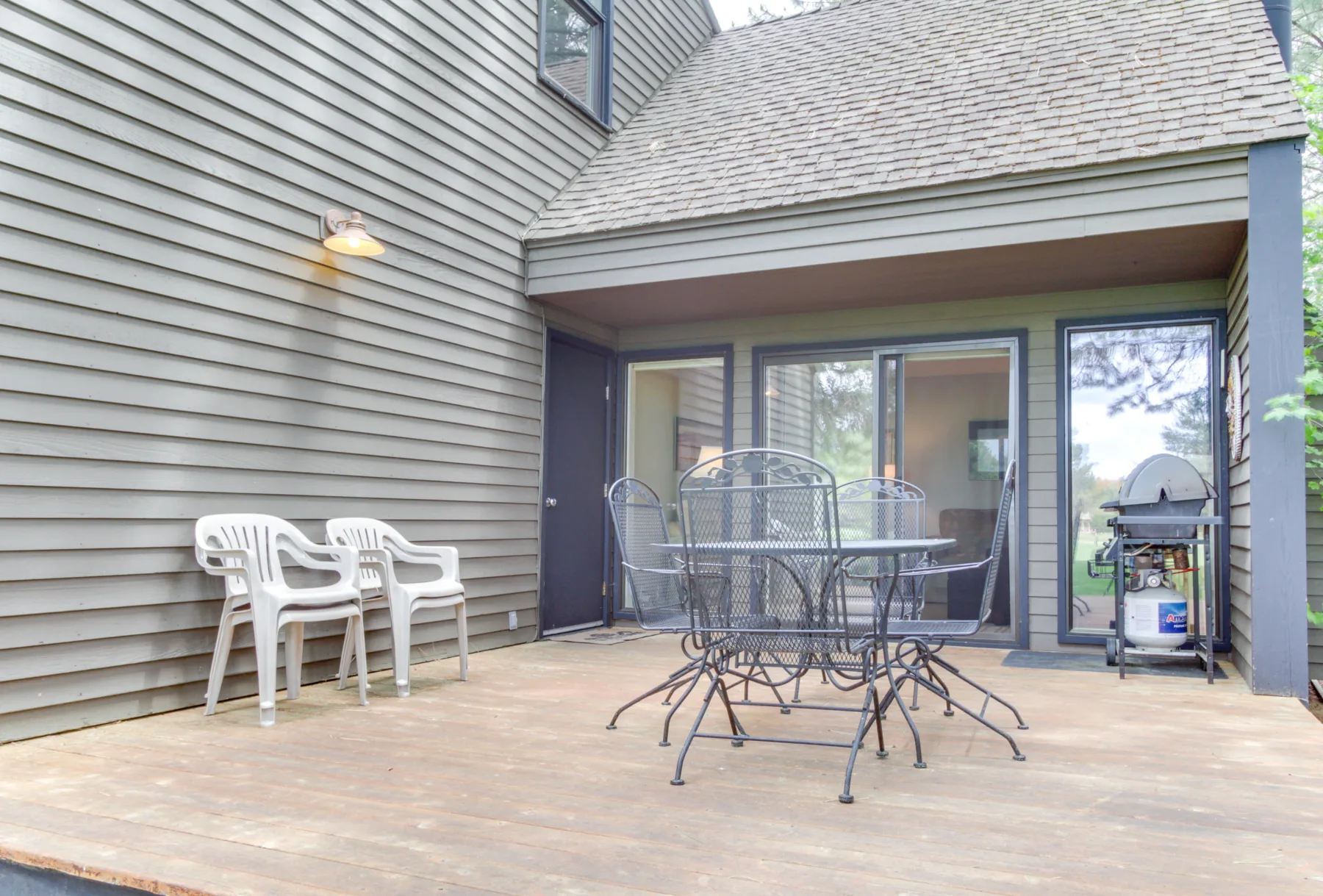 Un patio exterior con un conjunto de comedor de metal y asientos blancos de plástico.