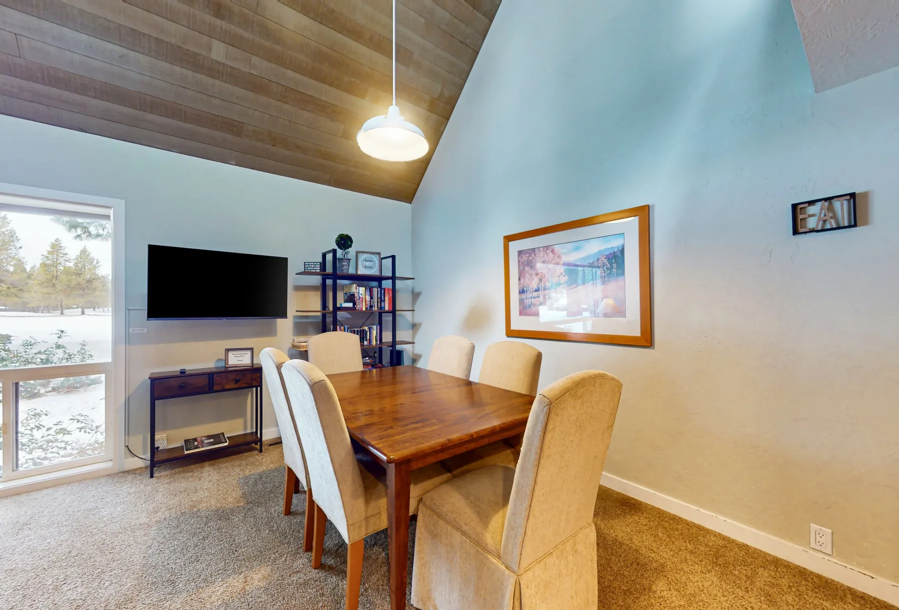Un comedor con una mesa de madera, asientos tapizados y un televisor.
