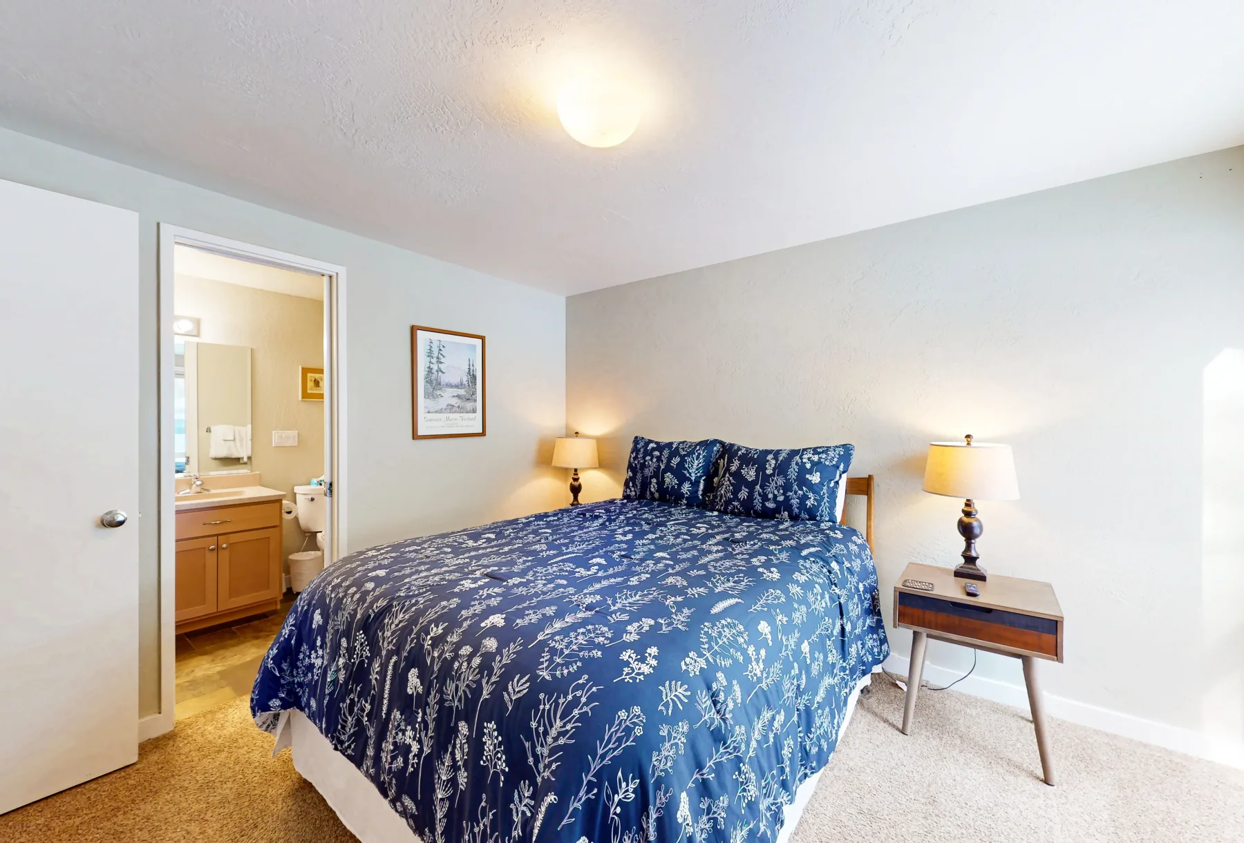 Un dormitorio con una cama cubierta con ropa de cama azul floral y mesitas de noche a juego.