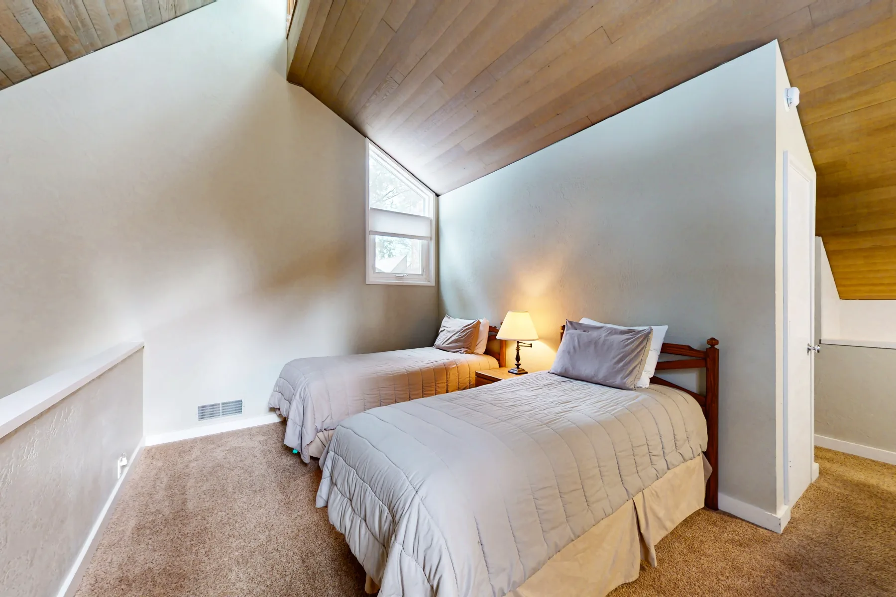 Dormitorio con dos camas, una lámpara de noche y un techo inclinado de madera.