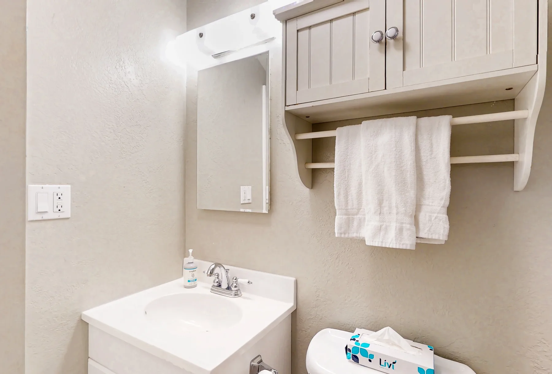 Un tocador de baño con lavabo, espejo de pared y armario encima.