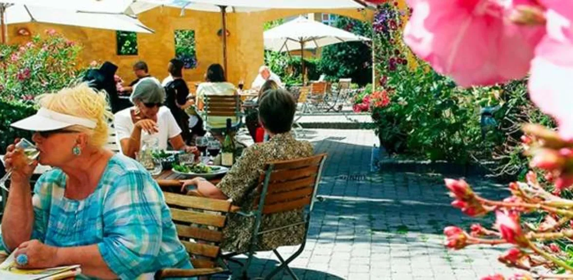 Representative hotel space: Outdoor patio dining area with seated people, tables, and garden plants.