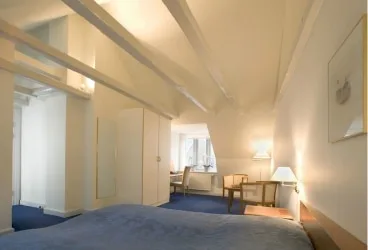 Representative hotel space: A bedroom with a bed, seating area, and exposed ceiling beams.