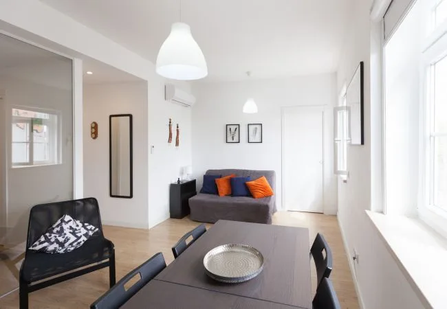 A bright living and dining area with a gray sofa and dark dining table.