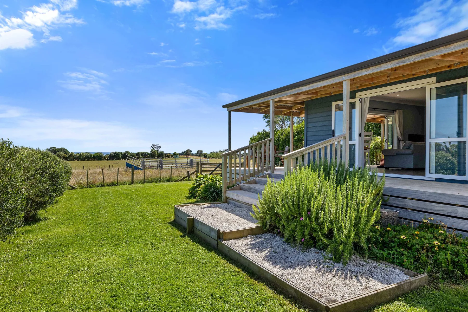 A house opens onto a green lawn and garden through a covered porch.