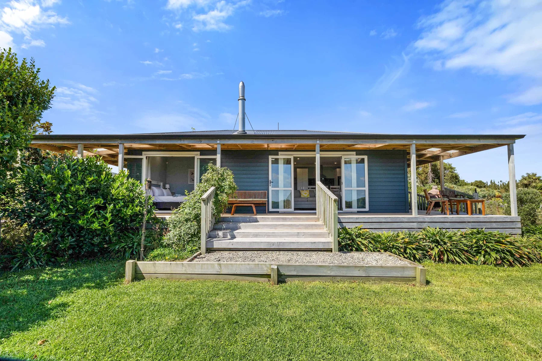 A single-story house with a broad covered porch and steps opens onto a green lawn.
