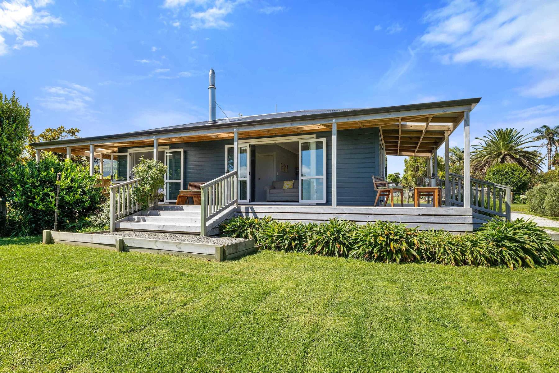 A raised house with a covered deck overlooks a broad green lawn.