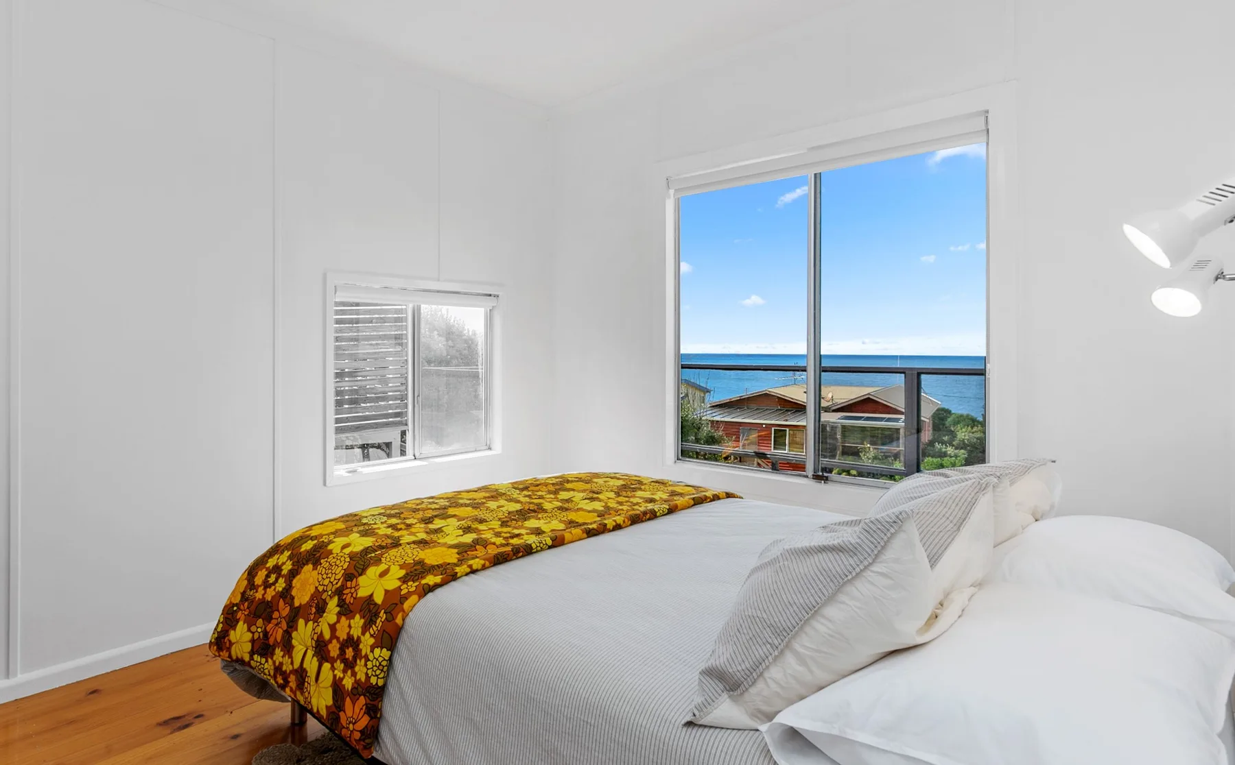 A bedroom with a bed and large windows overlooking the ocean.