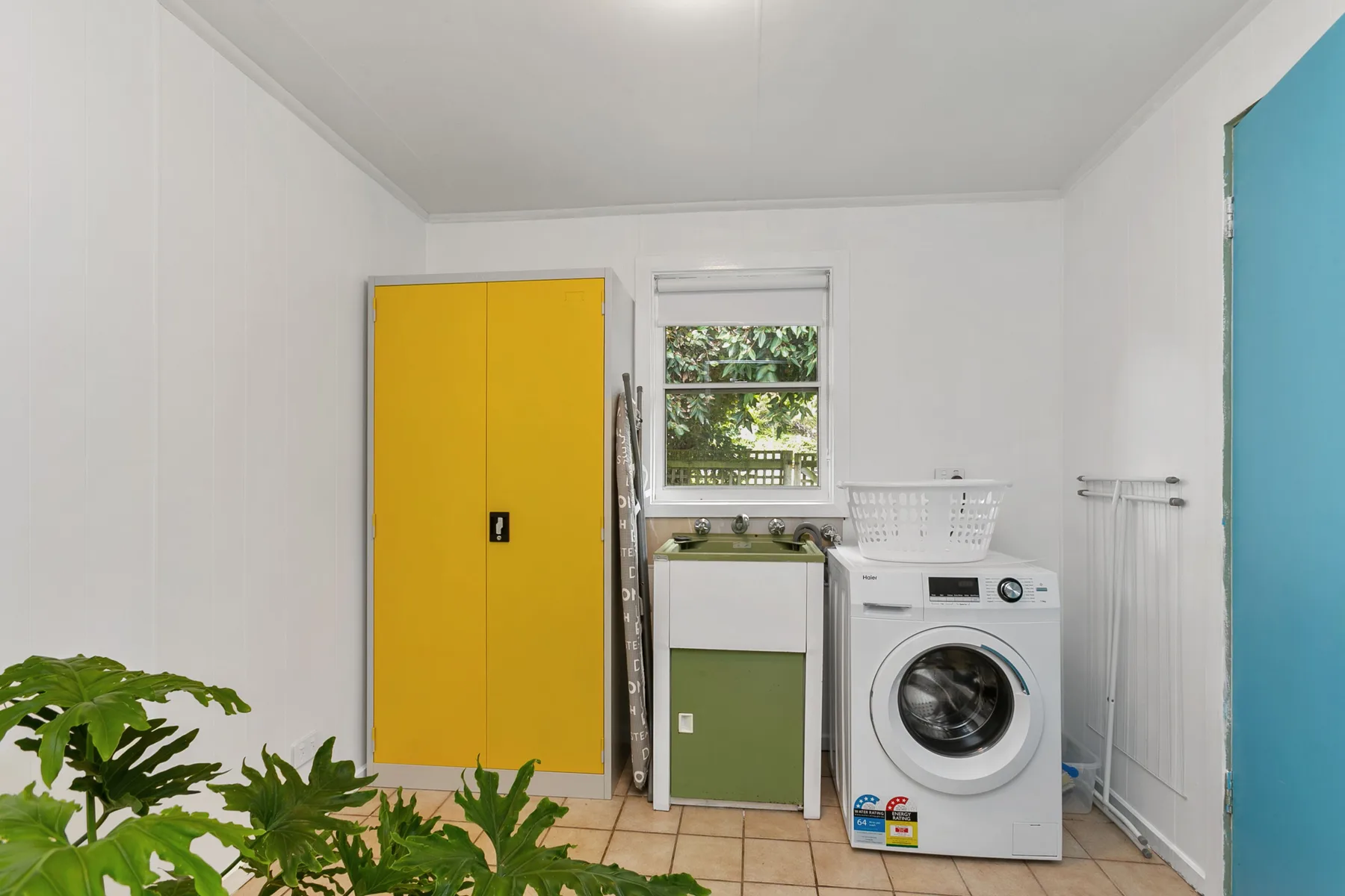 A laundry room with a washing machine beside a yellow cabinet.