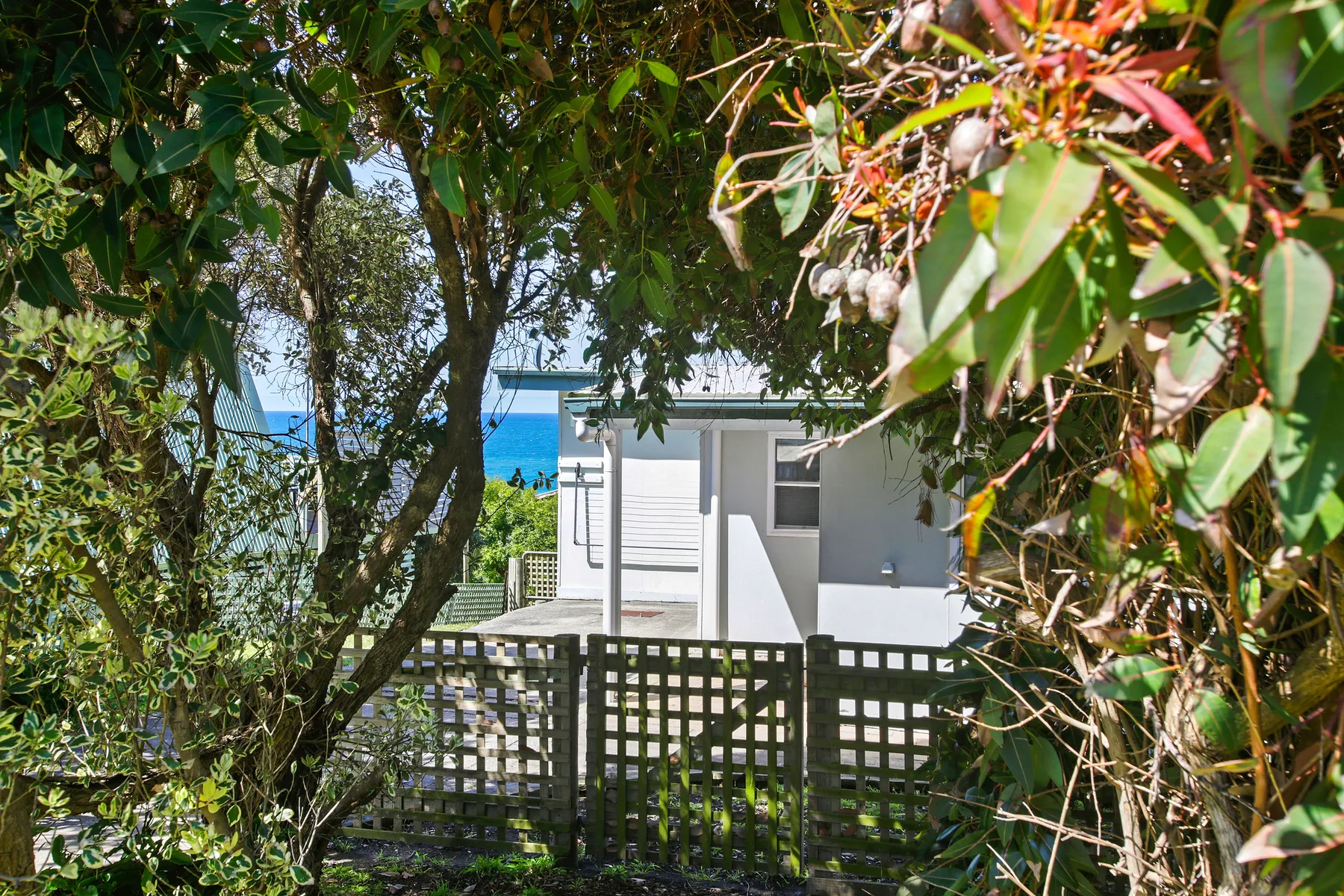 A small white building sits behind a wooden fence amid leafy greenery.