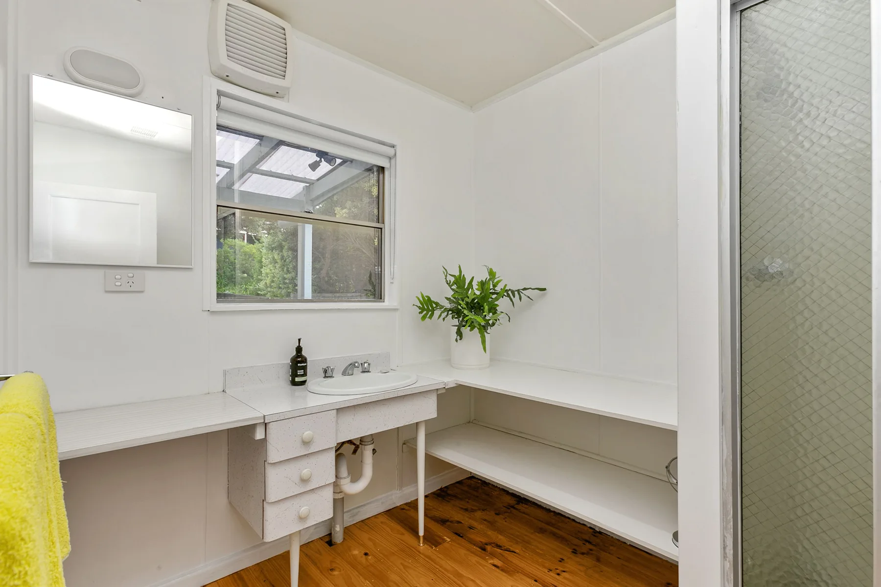 A bright bathroom with a long white countertop and a window.