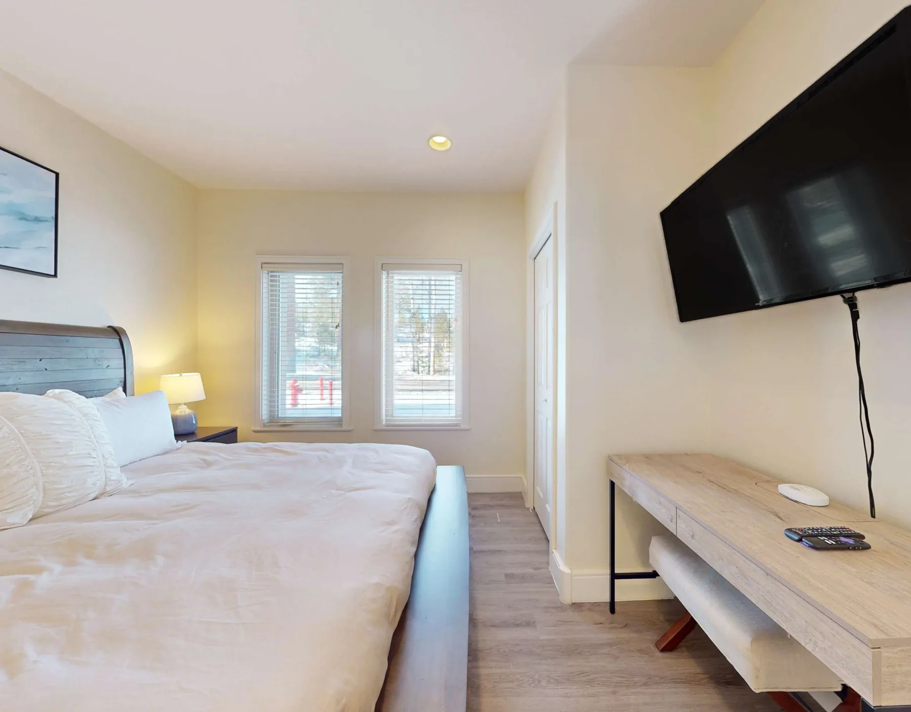 Un dormitorio con una cama, dos ventanas y un televisor montado en la pared.