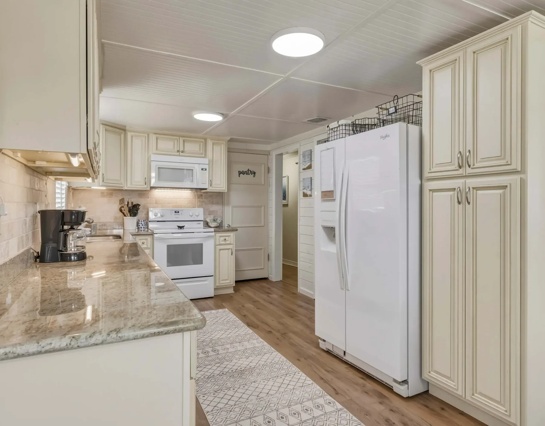 A bright kitchen with light cabinetry, a large refrigerator, and a stone countertop.