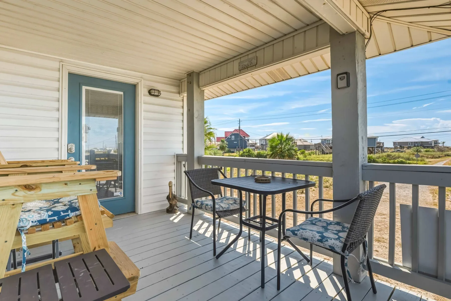 A covered porch with a table and seating overlooks a sunny outdoor area.