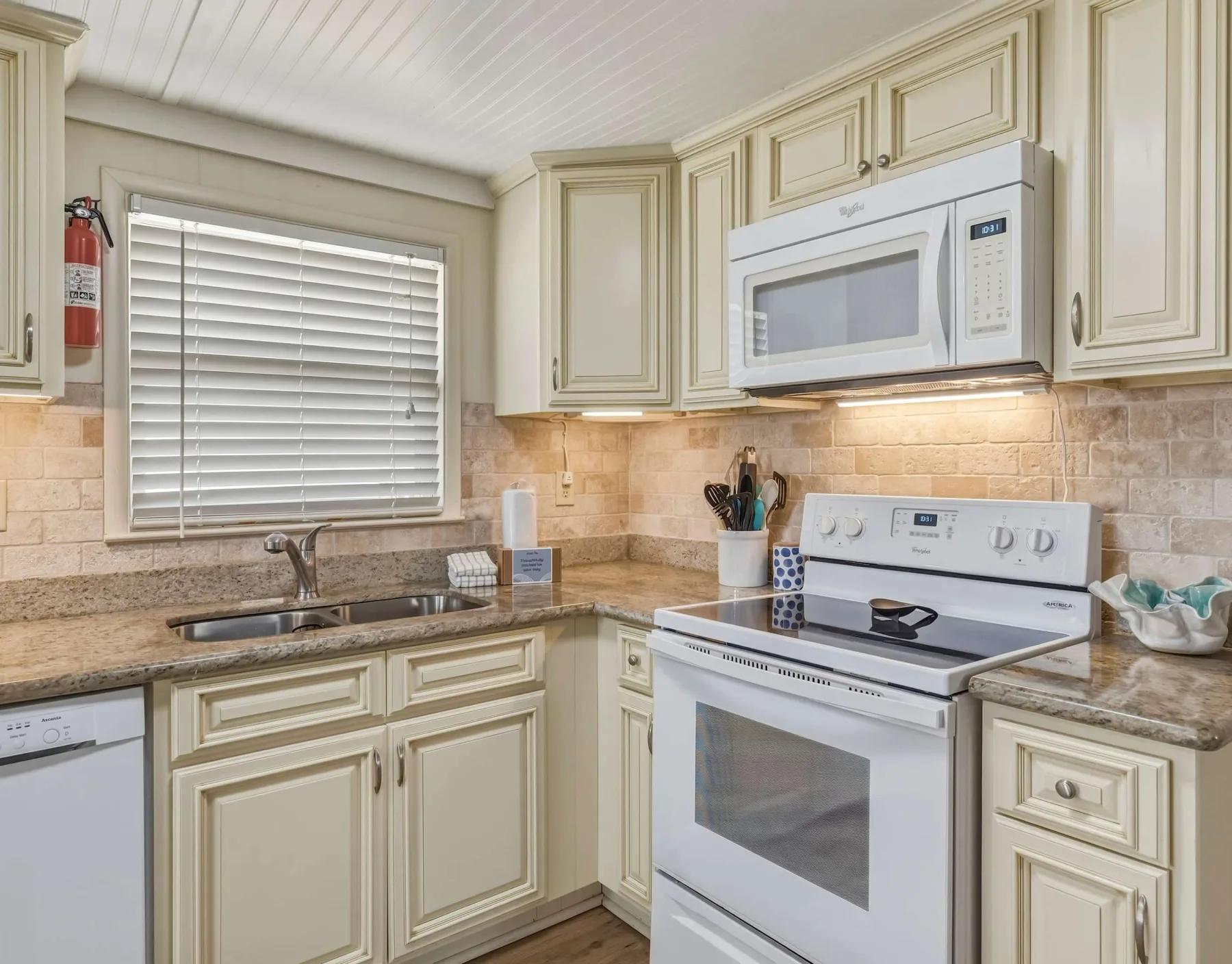 A bright kitchen with cream cabinets, a countertop, and white appliances.
