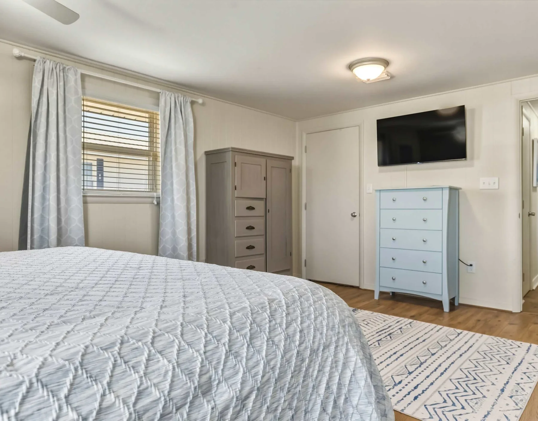 A bedroom with a bed, two dressers, and a wall-mounted television.
