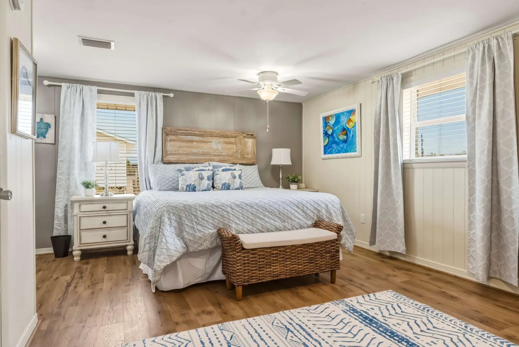 A bedroom with a bed, bedside tables, and windows with light curtains.