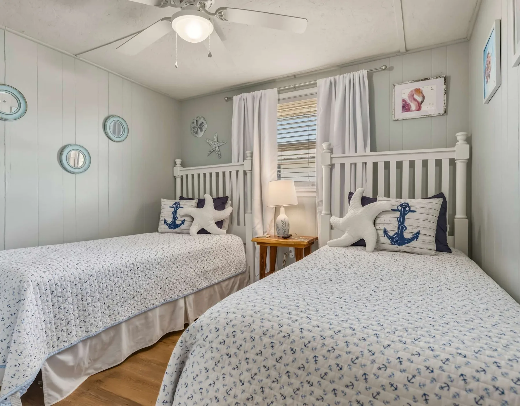 A bedroom with two beds, nautical-patterned bedding, and a small table between them.