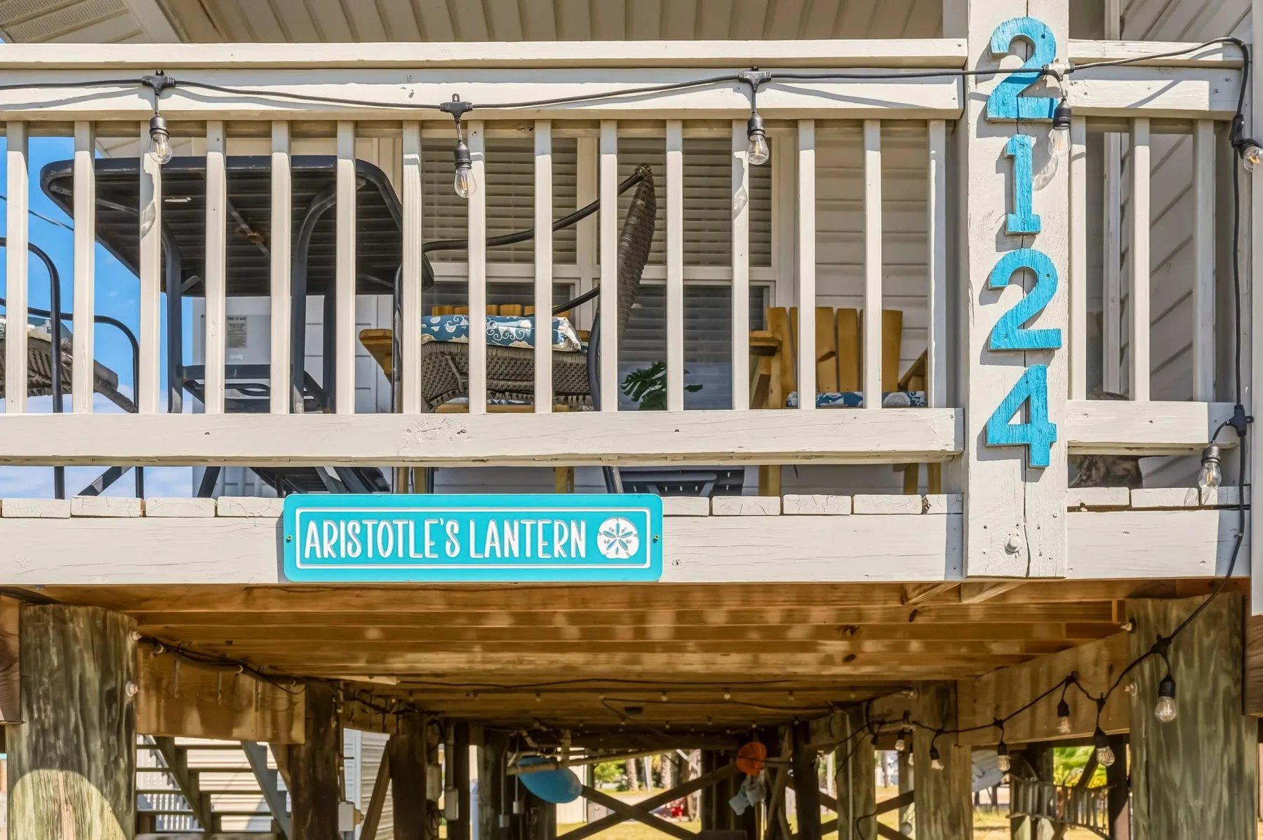 A raised wooden deck with white railings and a turquoise sign.