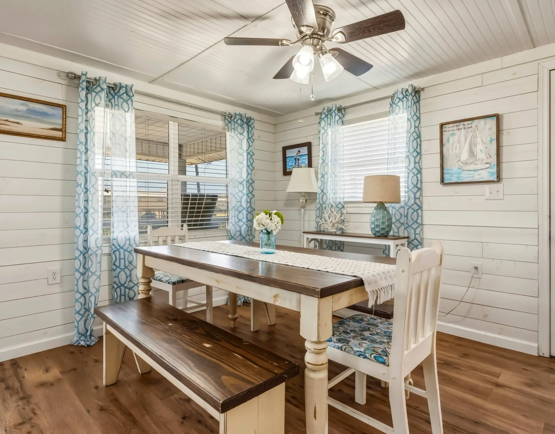 A bright dining room with a long table, benches, and blue patterned curtains.