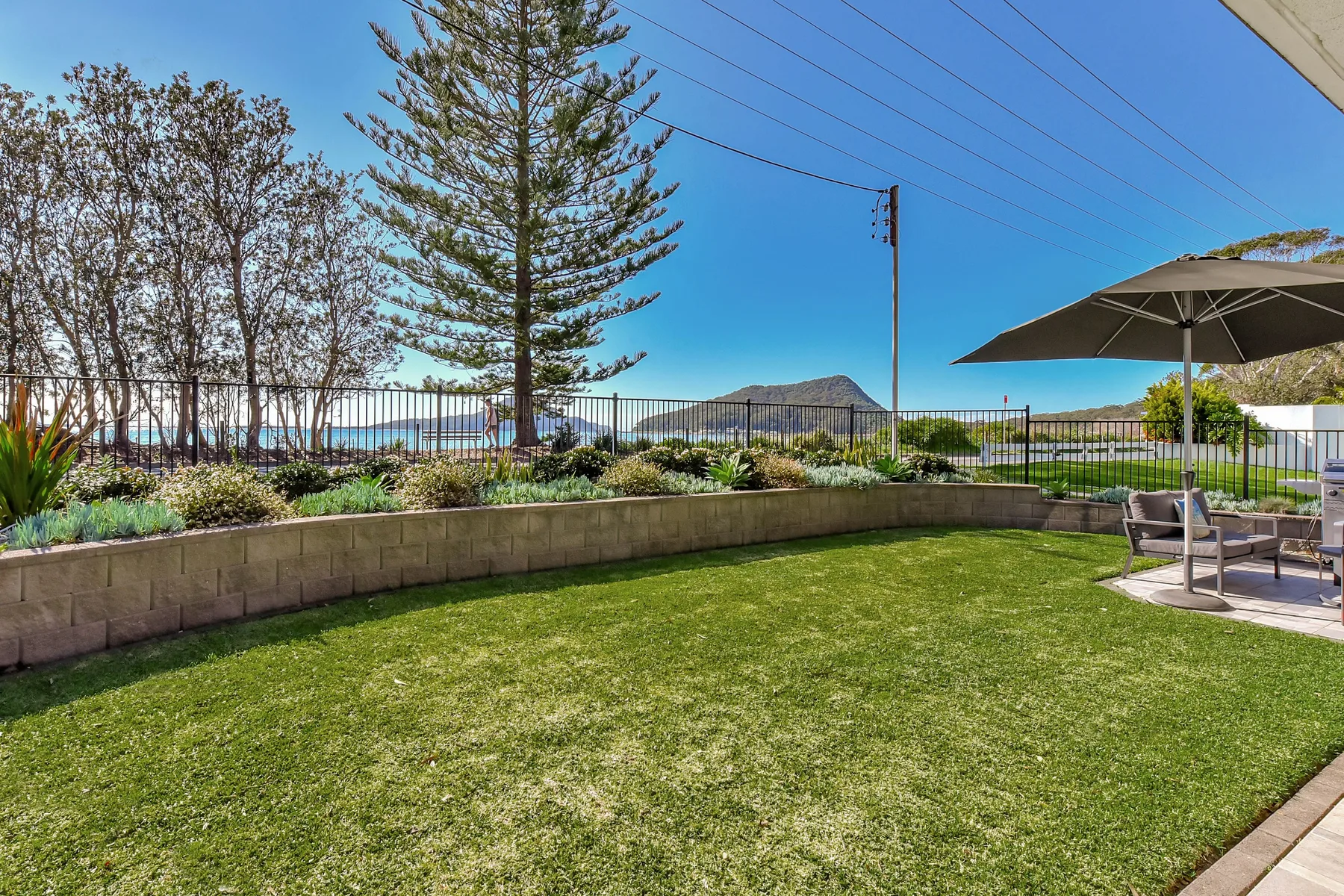A grassy garden with a planted border, outdoor seating, and distant water.