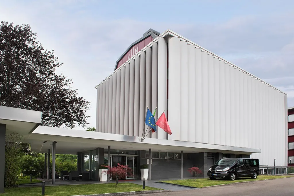 Espacio representativo del hotel: Exterior de un hotel moderno con una entrada cubierta y banderas.