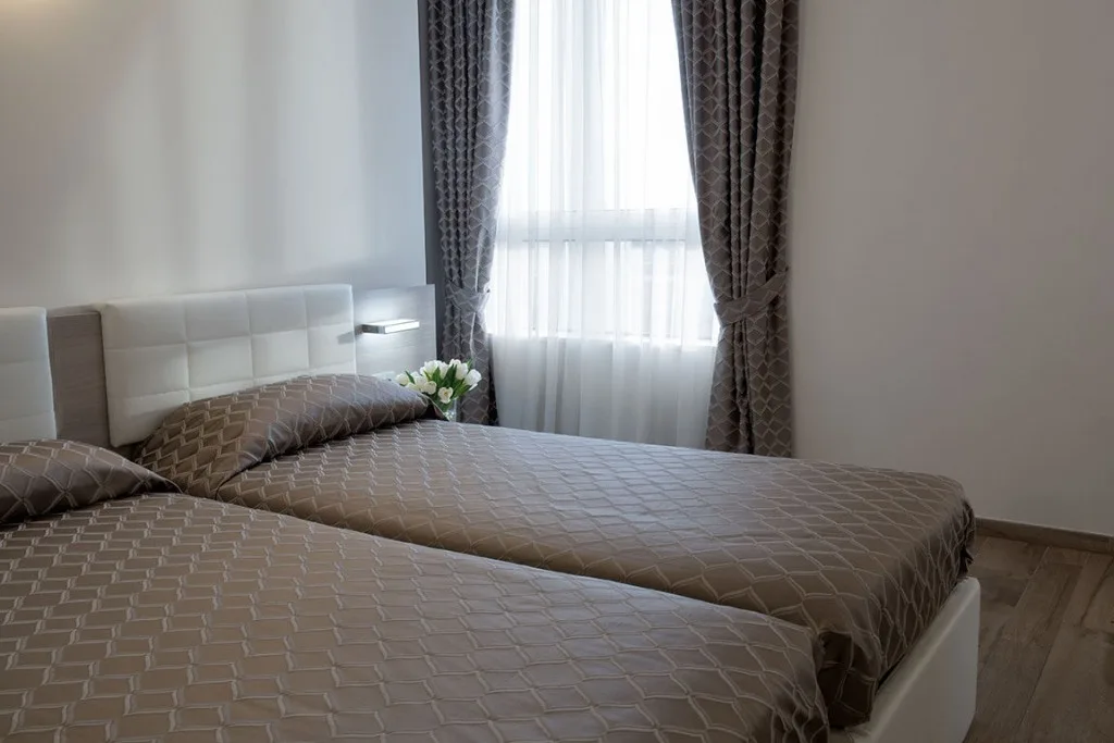 Espacio representativo del hotel: Un dormitorio con dos camas junto a una ventana con cortinas.