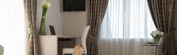 Espacio representativo del hotel: Una sala de estar con televisión, asientos y una amplia ventana con cortinas.